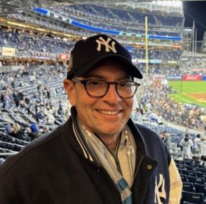 color photo of Marc Wigder wearing a baseball hat and jacket in front of a crowd